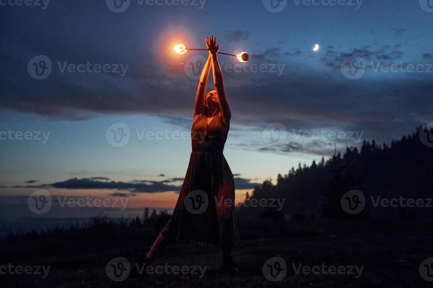 Fire show by woman in dress in night Carphatian mountains. Beautiful landscape photo