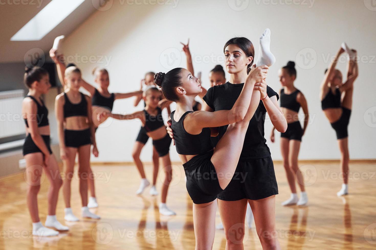 With help from coach. Group of female kids practicing athletic exercises together indoors photo