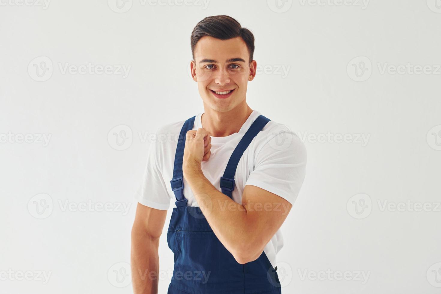 Shows biceps. Ready to work. Male worker in blue uniform standing inside of studio against white background photo