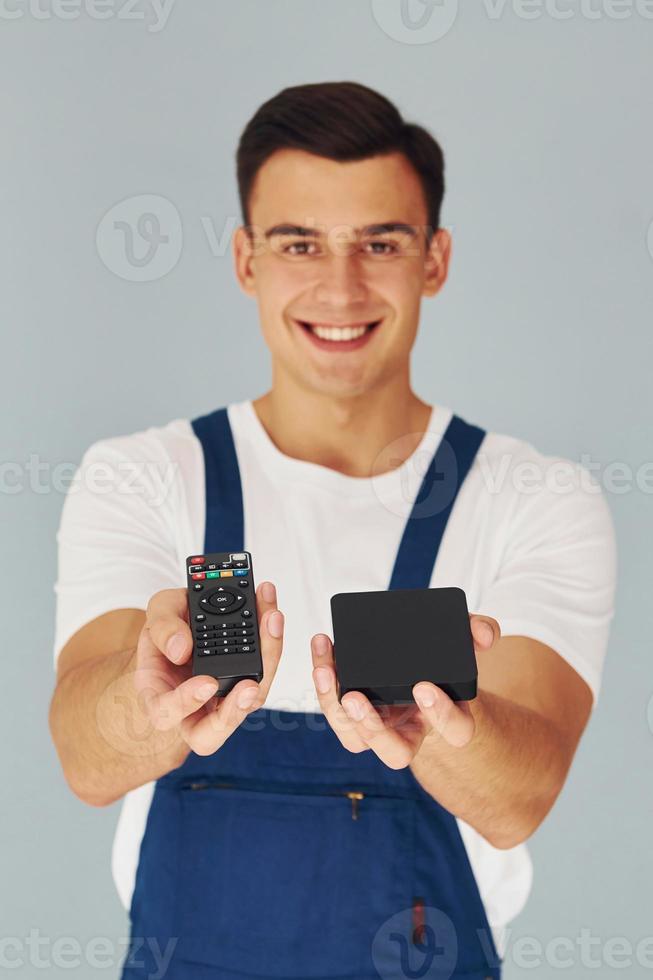 TV remote controller and smartphone. Male worker in blue uniform standing inside of studio against white background photo