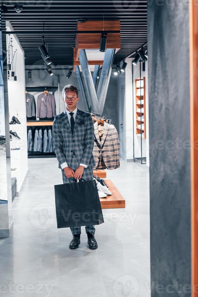 chico joven en una tienda moderna con ropa nueva. ropa elegante y cara para hombres foto