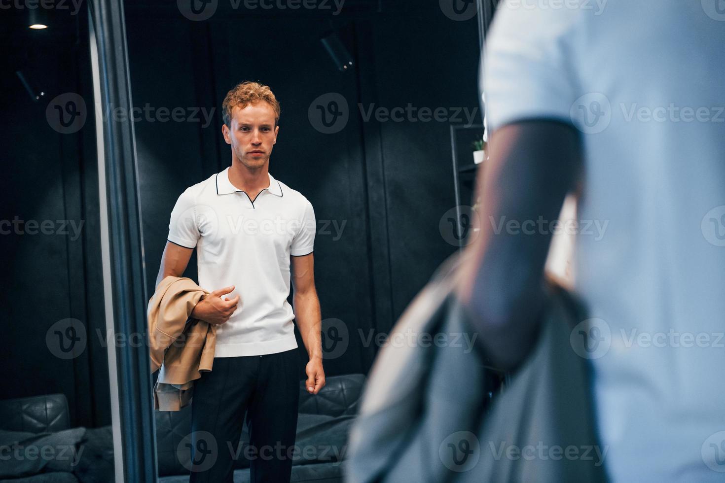 Guy in white shirt tries on new clothes and looks in the mirror photo