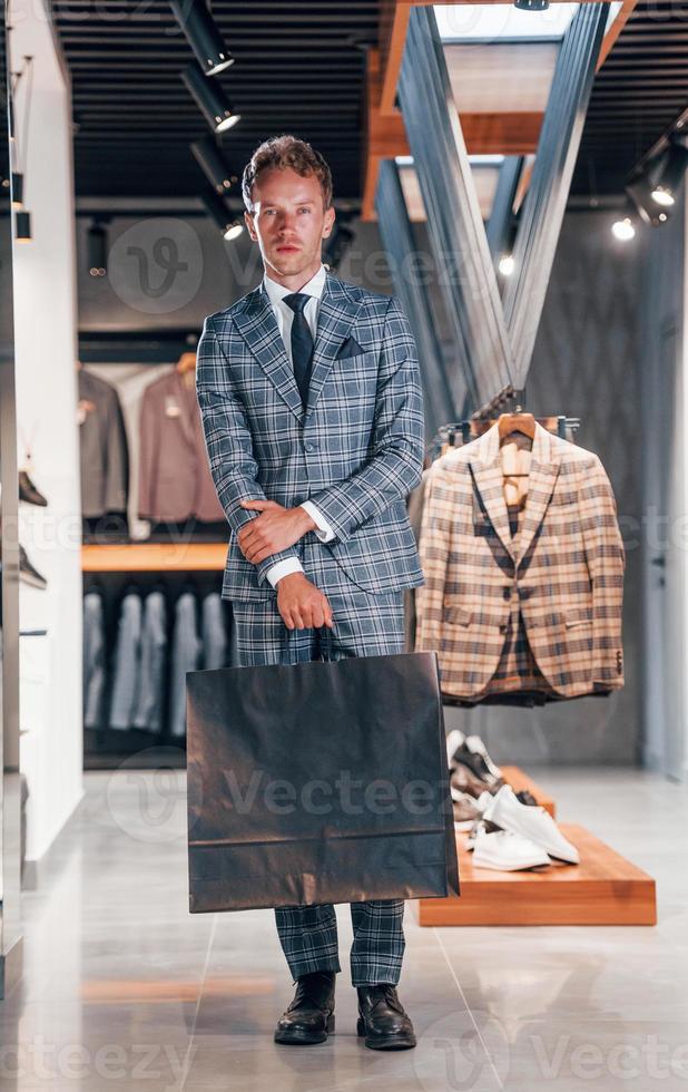 chico joven en una tienda moderna con ropa nueva. ropa elegante y cara para hombres foto
