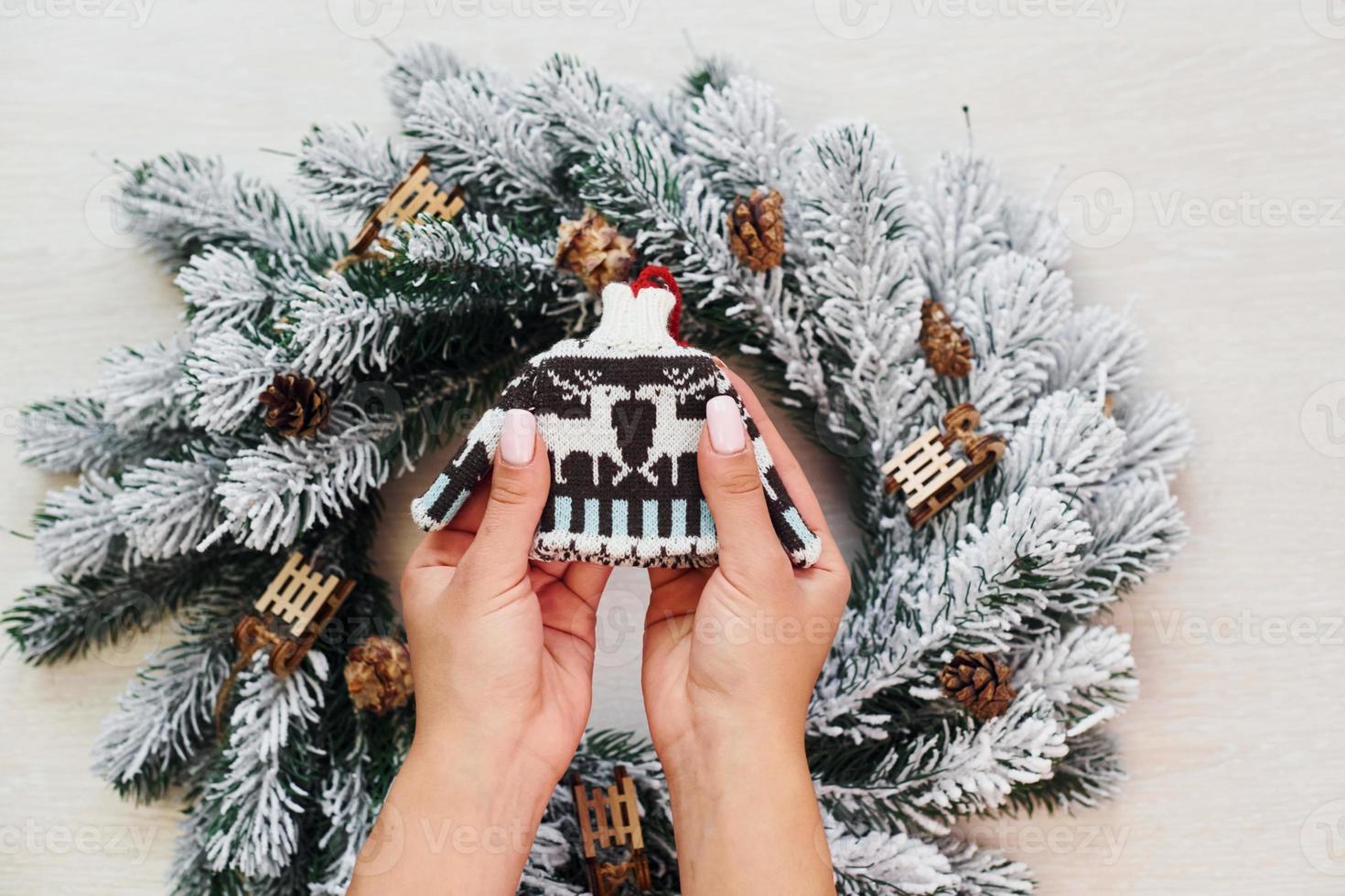 Woman's hands holds little sweater. Top view of christmas festive texture with new year decorations photo