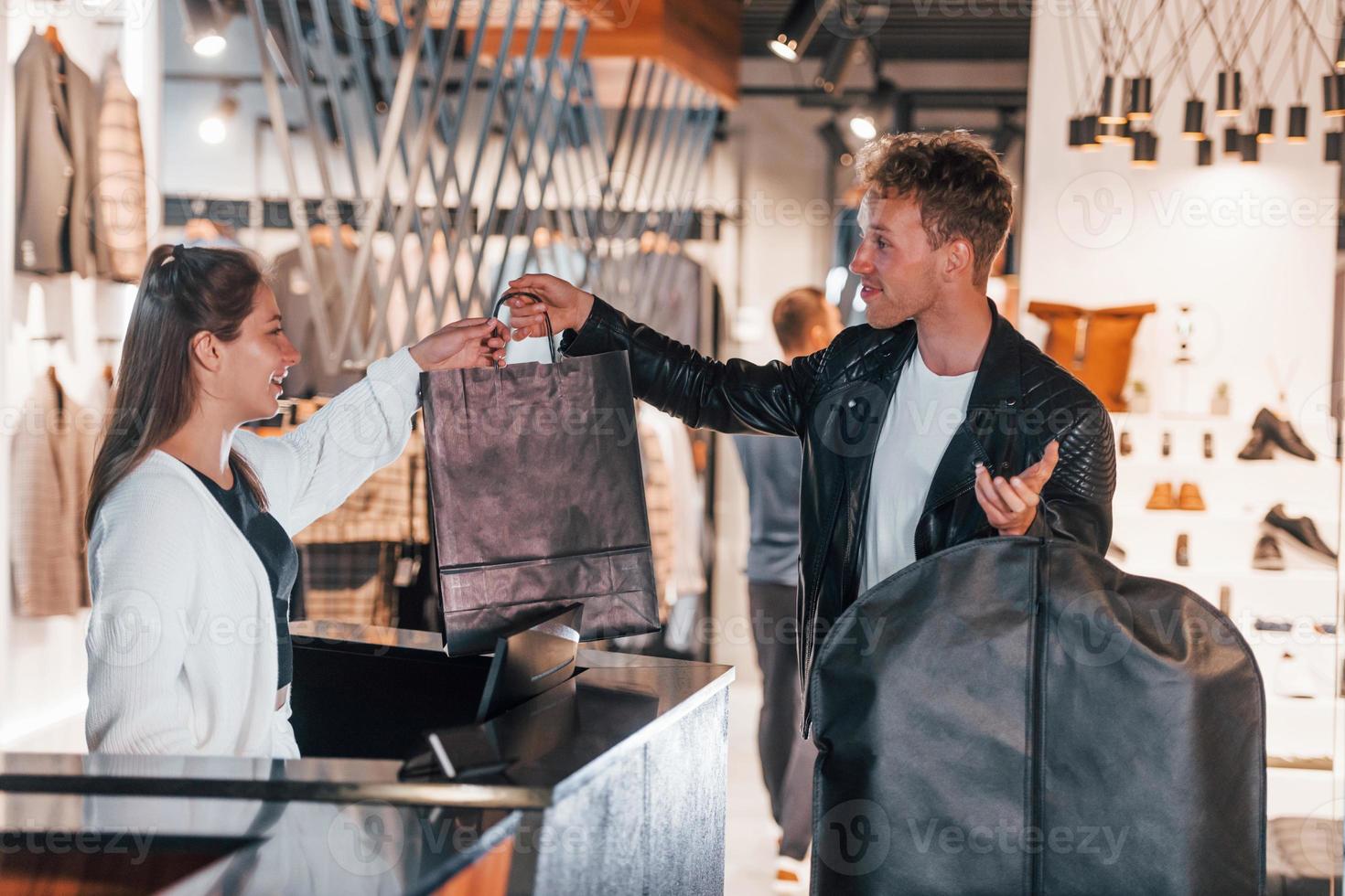 Man makes purchase in modern store with elegant clothes. Female