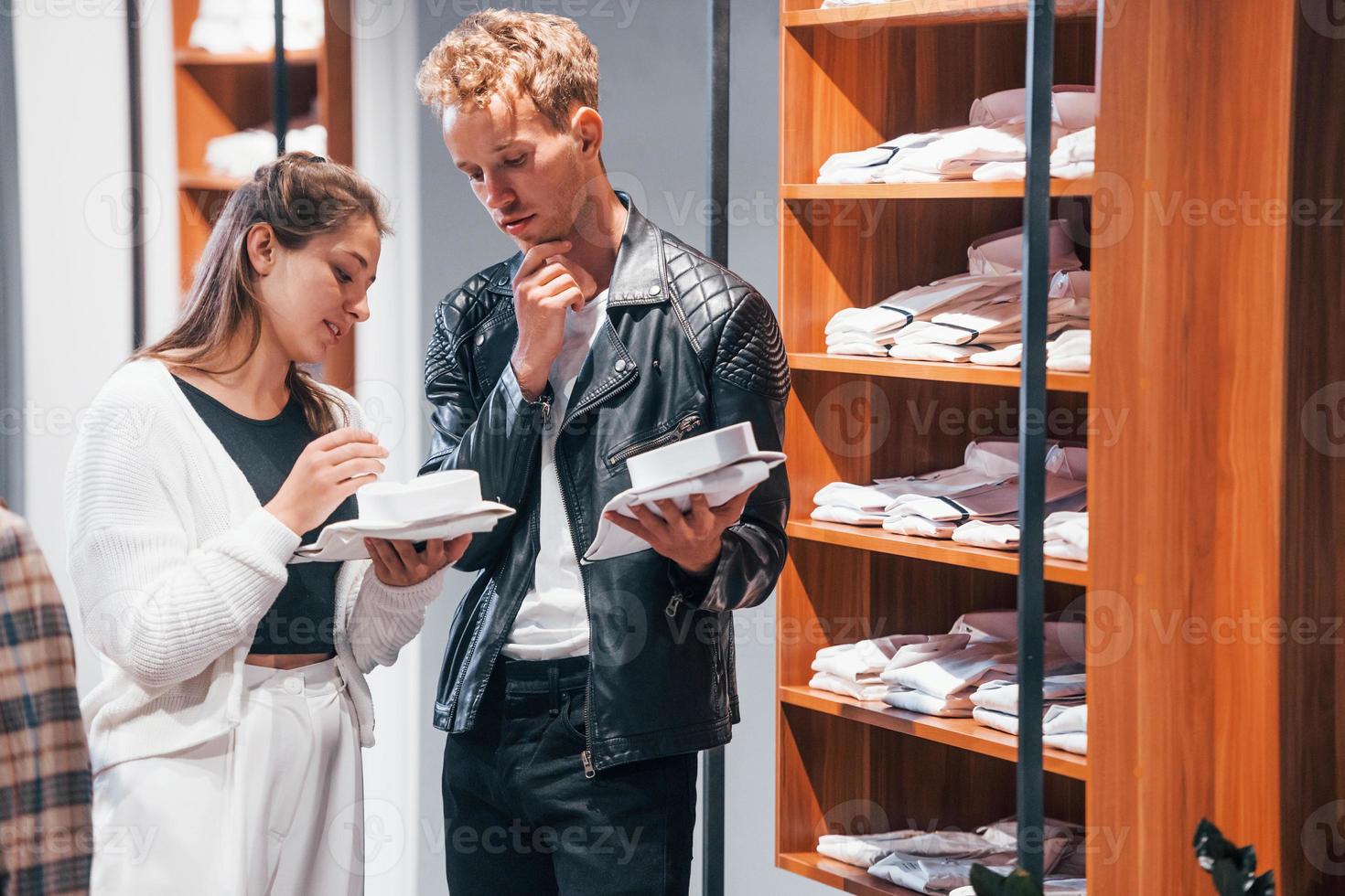 joven trabajadora ayudando a un chico a elegir ropa en una tienda moderna con ropa cara para hombres foto