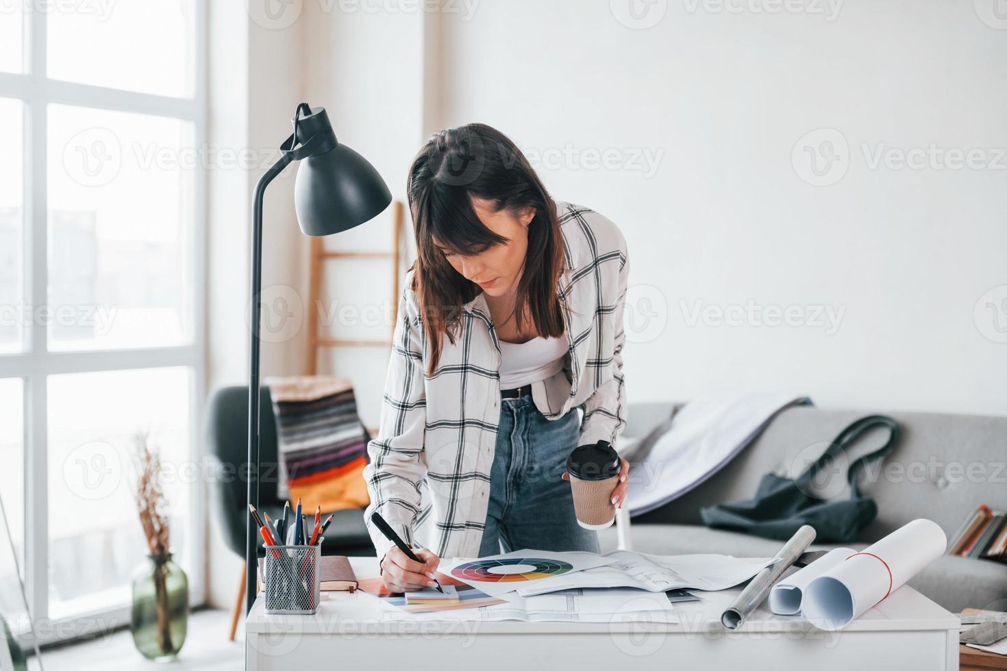 Standing near table. Young female freelance worker is indoors in home at daytime photo
