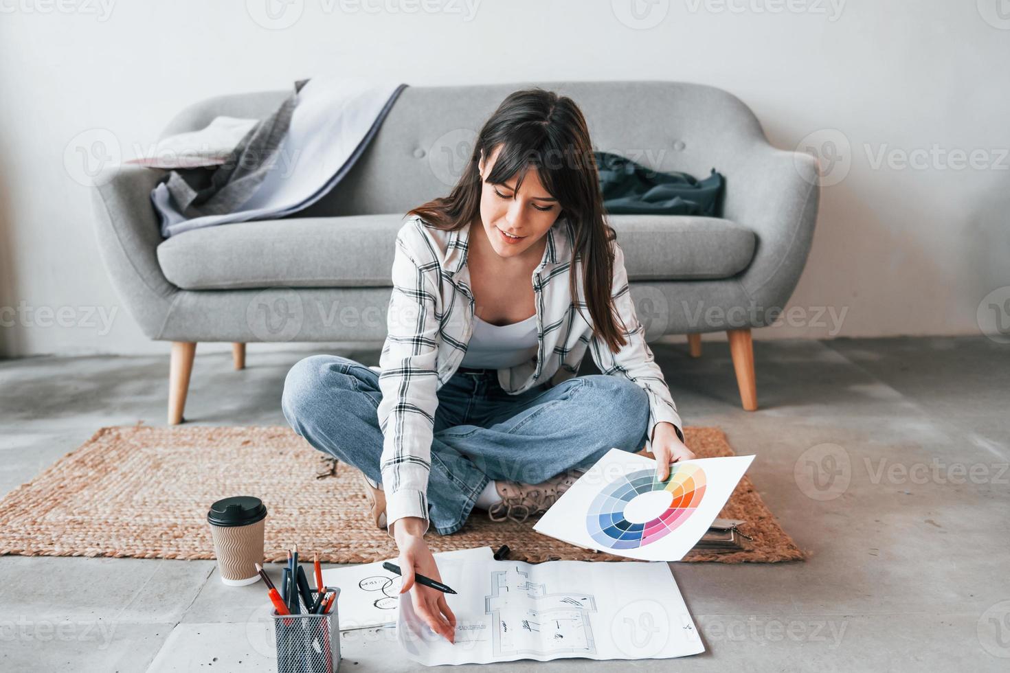 Sits on the floor. Young female freelance worker is indoors in home at daytime photo