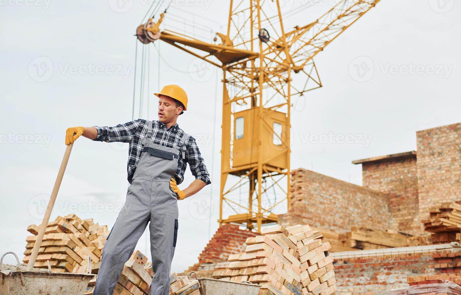 Using shovel with wooden holder. Construction worker in uniform and safety equipment have job on building photo