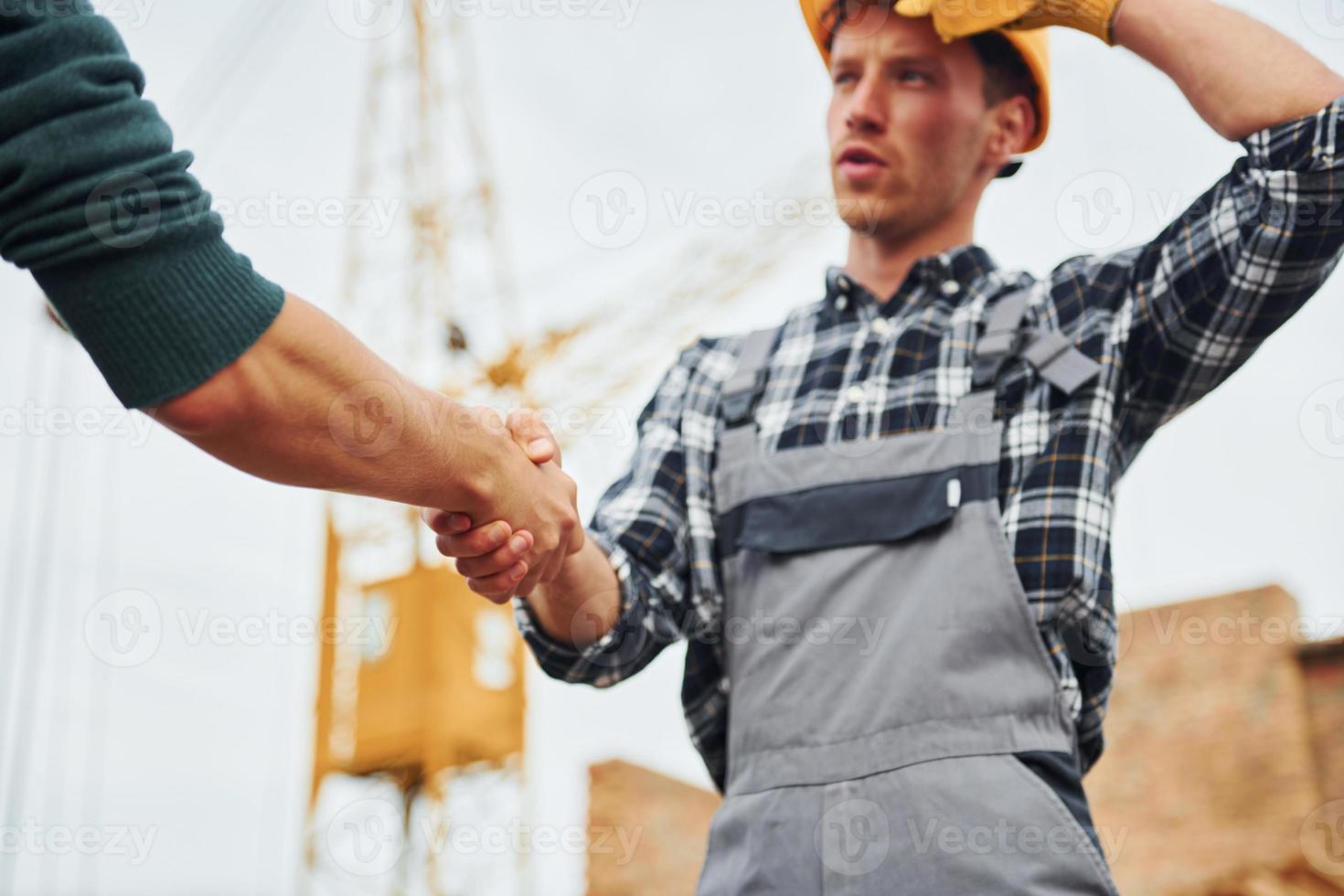 Making handshake. Two construction workers in uniform and safety equipment have job on building together photo