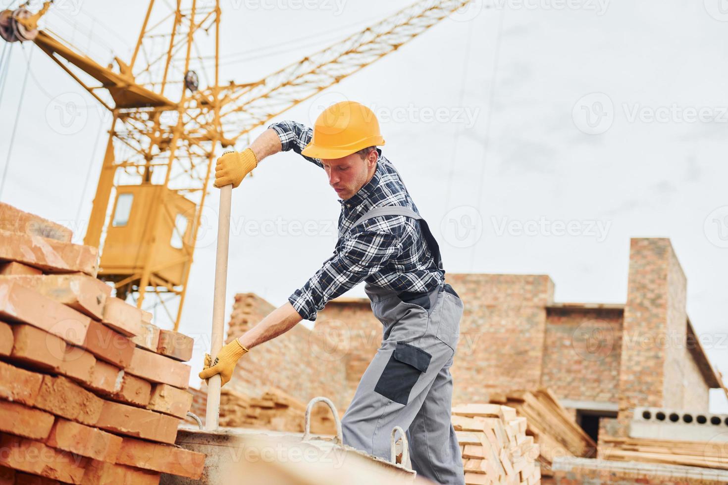 With shovel in hands. Construction worker in uniform and safety equipment have job on building photo