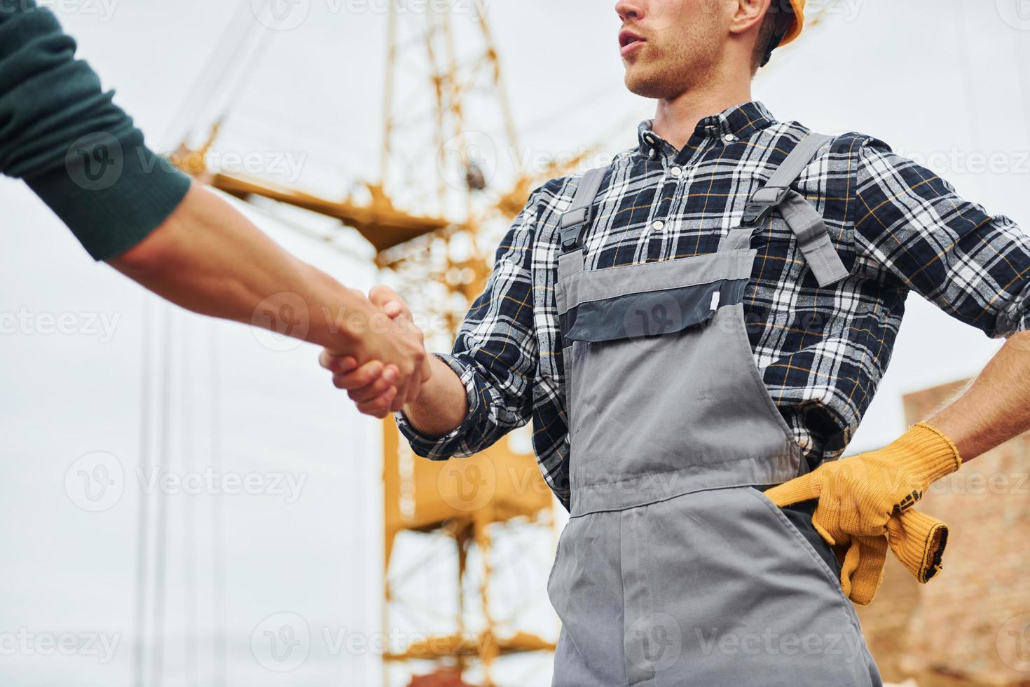 Making handshake. Two construction workers in uniform and safety equipment have job on building together photo