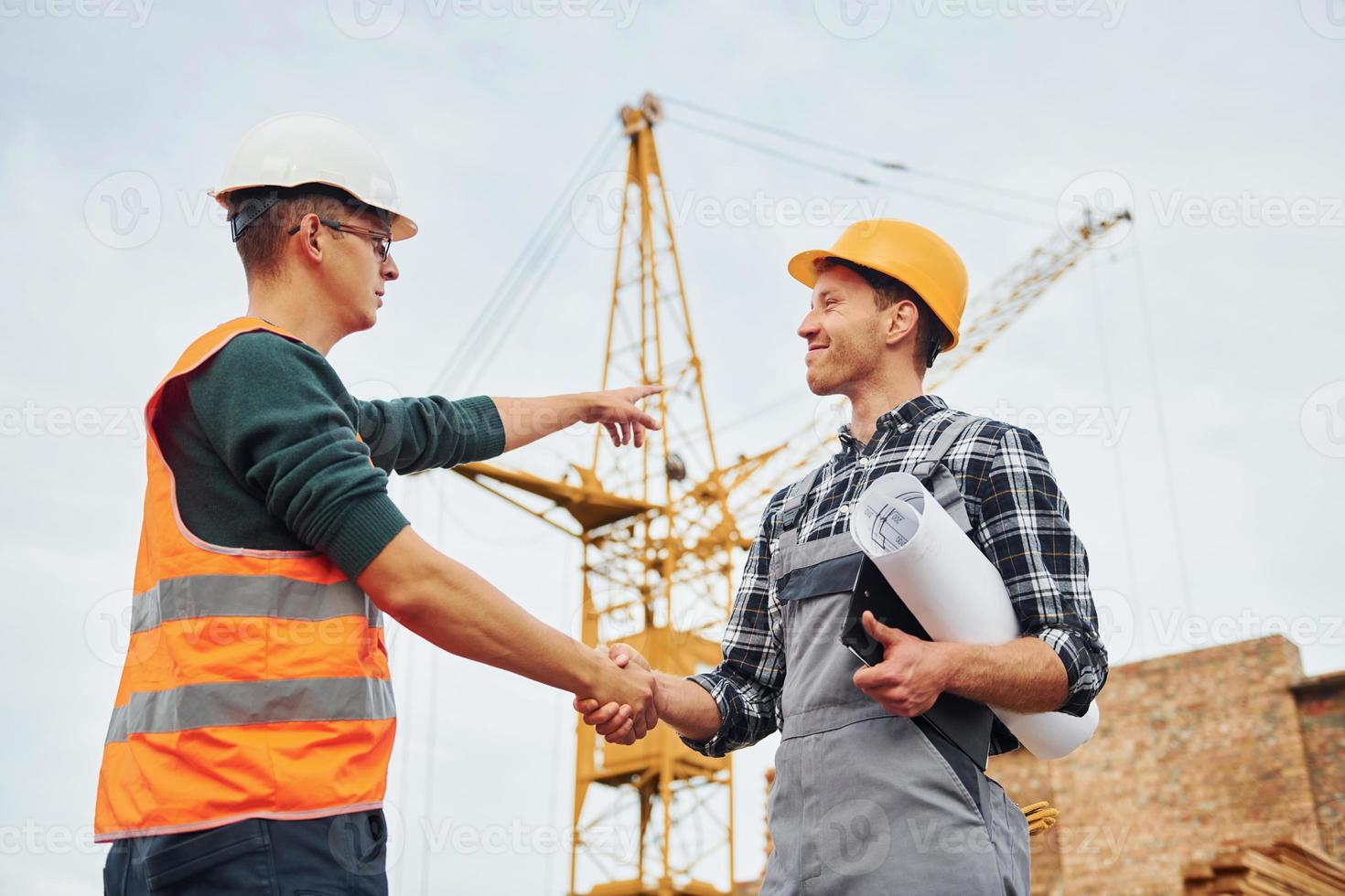 Making handshake. Two construction workers in uniform and safety equipment have job on building together photo