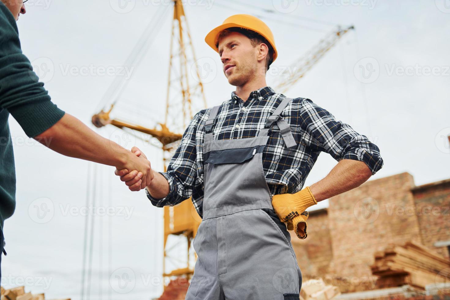 Making handshake. Two construction workers in uniform and safety equipment have job on building together photo
