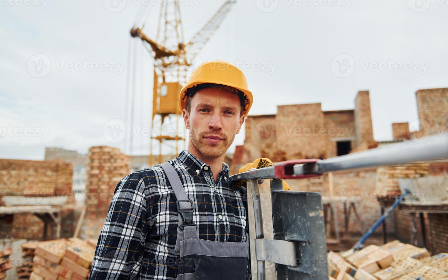 Ladder in hands. Construction worker in uniform and safety equipment have job on building photo