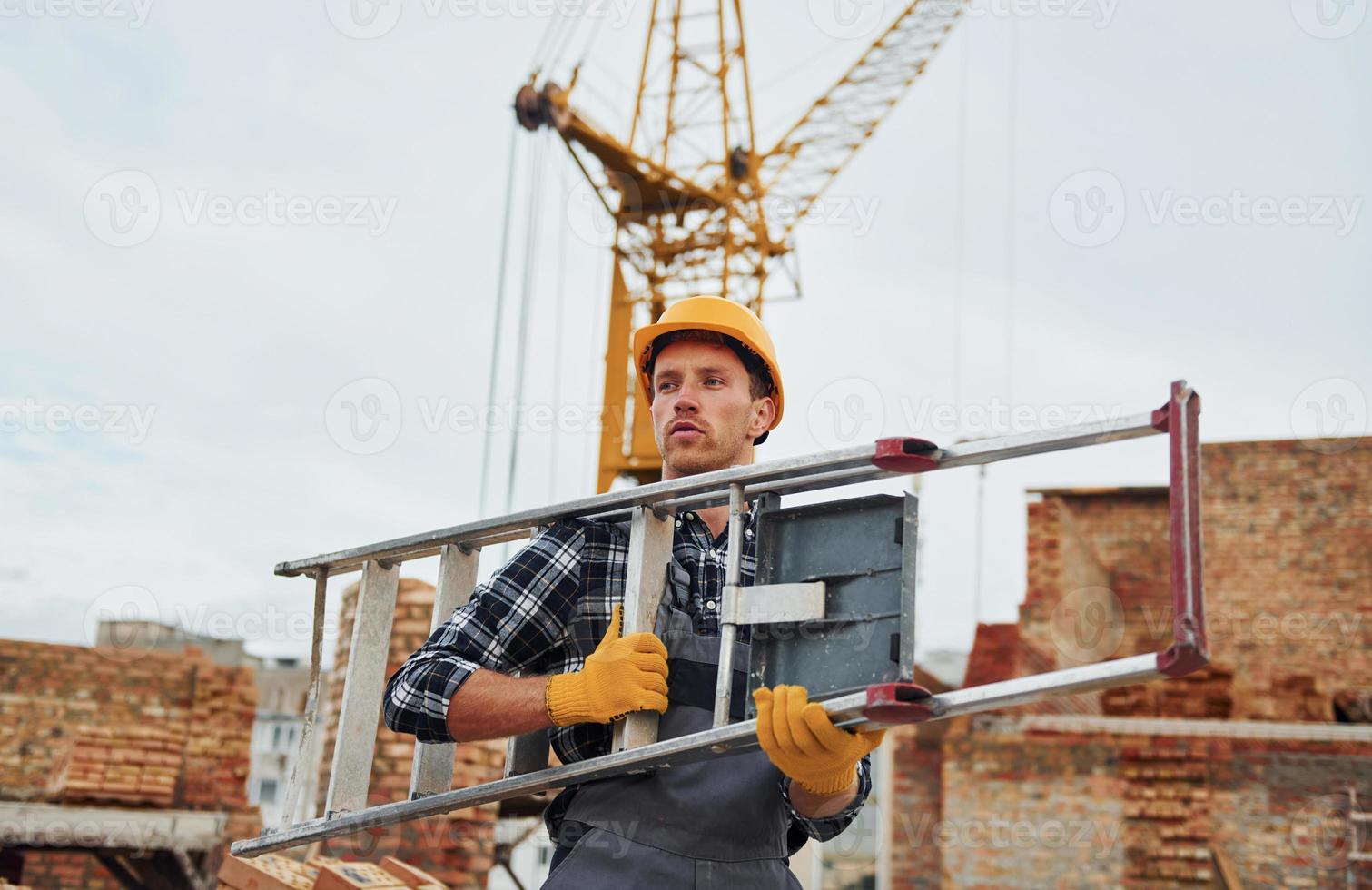 Ladder in hands. Construction worker in uniform and safety equipment have job on building photo