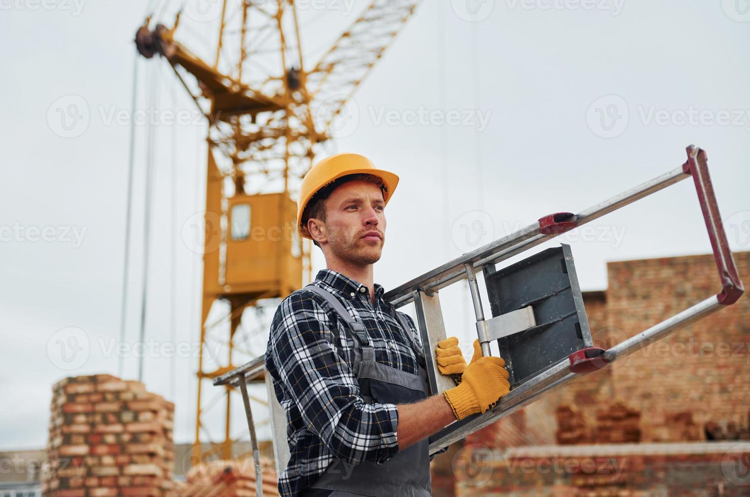 Ladder in hands. Construction worker in uniform and safety equipment have job on building photo