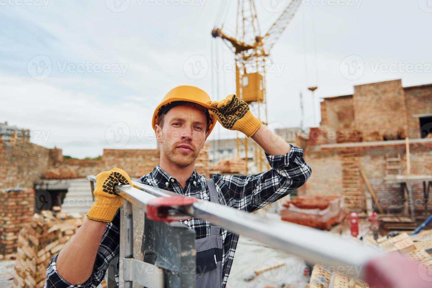 Ladder in hands. Construction worker in uniform and safety equipment have job on building photo