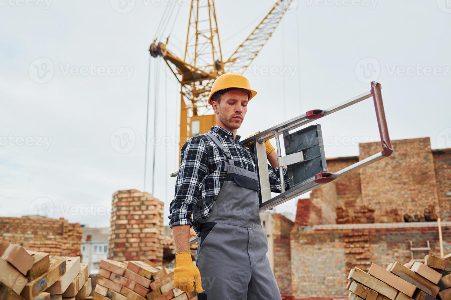 Ladder in hands. Construction worker in uniform and safety equipment have job on building photo