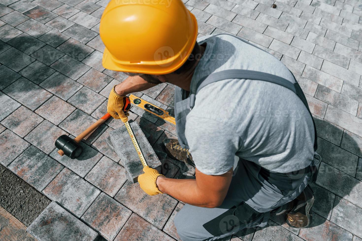 Measuring process. Male worker in yellow colored uniform have job with pavement photo