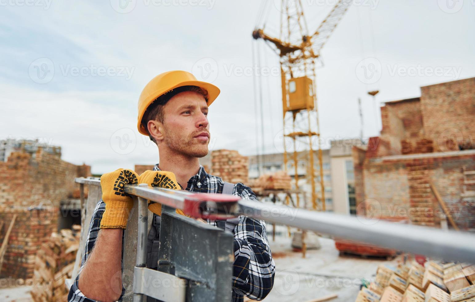 Ladder in hands. Construction worker in uniform and safety equipment have job on building photo