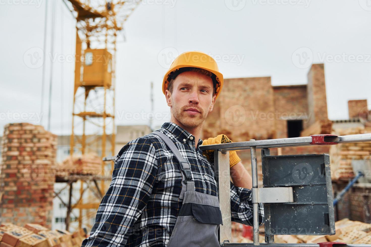 Ladder in hands. Construction worker in uniform and safety equipment have job on building photo