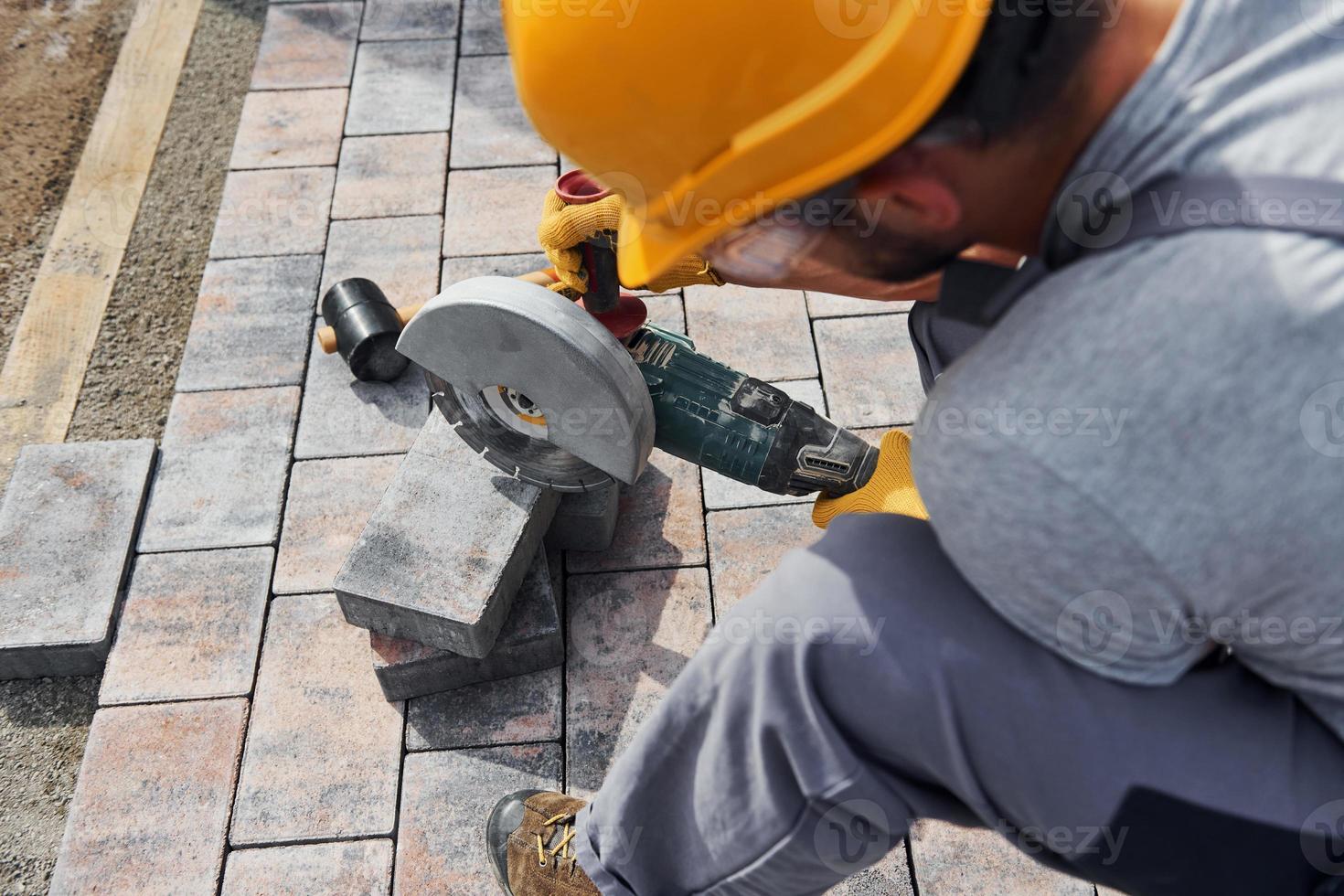 Close up view. Male worker in yellow colored uniform have job with pavement photo