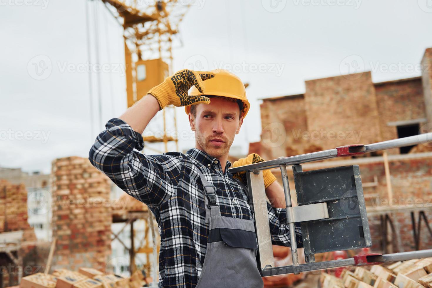 Ladder in hands. Construction worker in uniform and safety equipment have job on building photo
