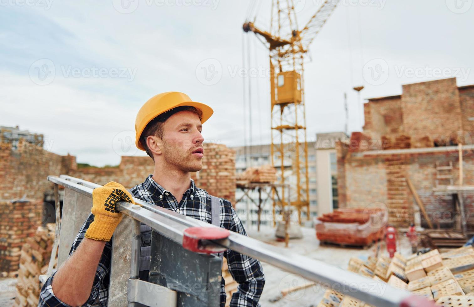 Ladder in hands. Construction worker in uniform and safety equipment have job on building photo