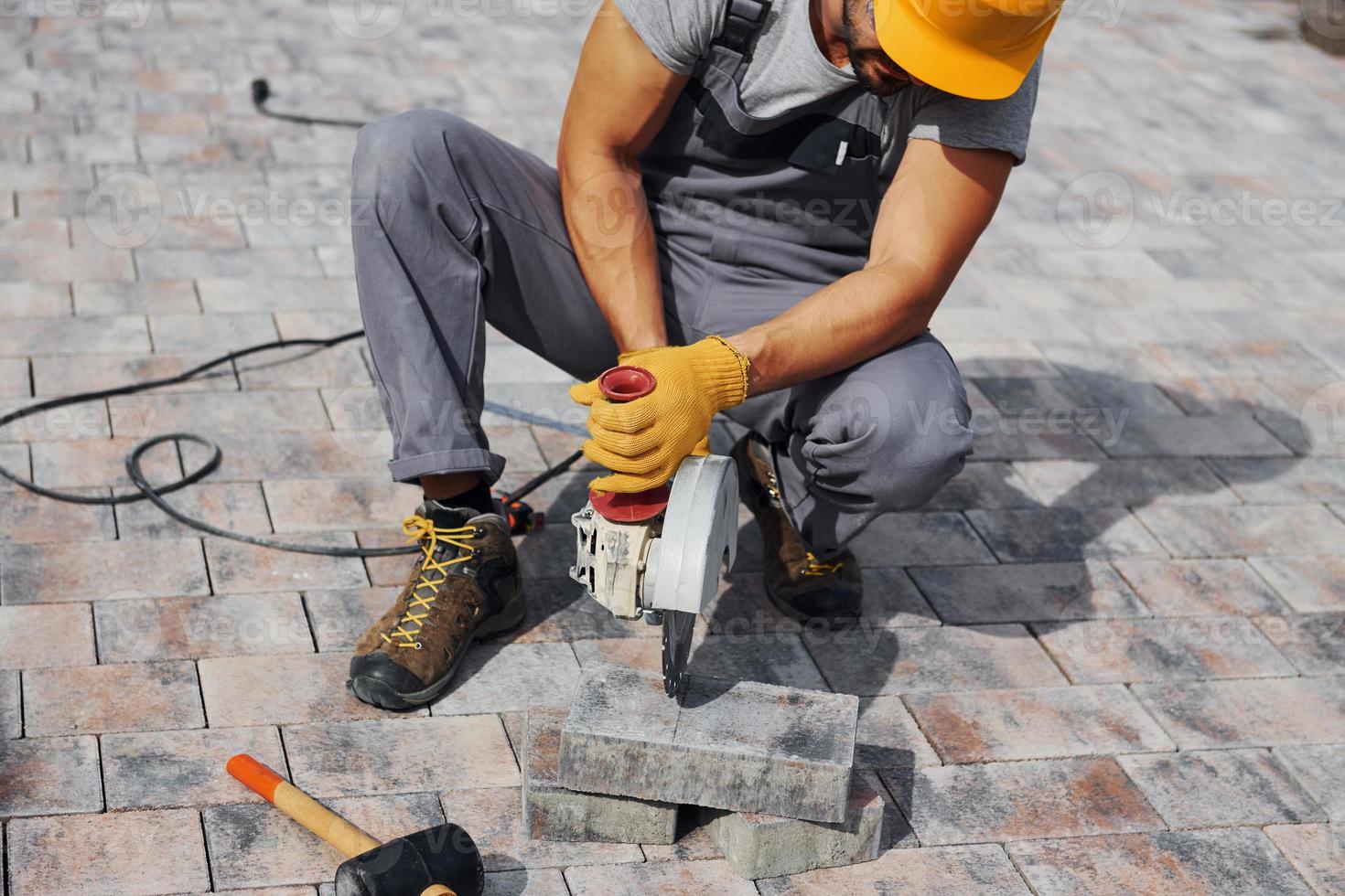 Close up view. Male worker in yellow colored uniform have job with pavement photo