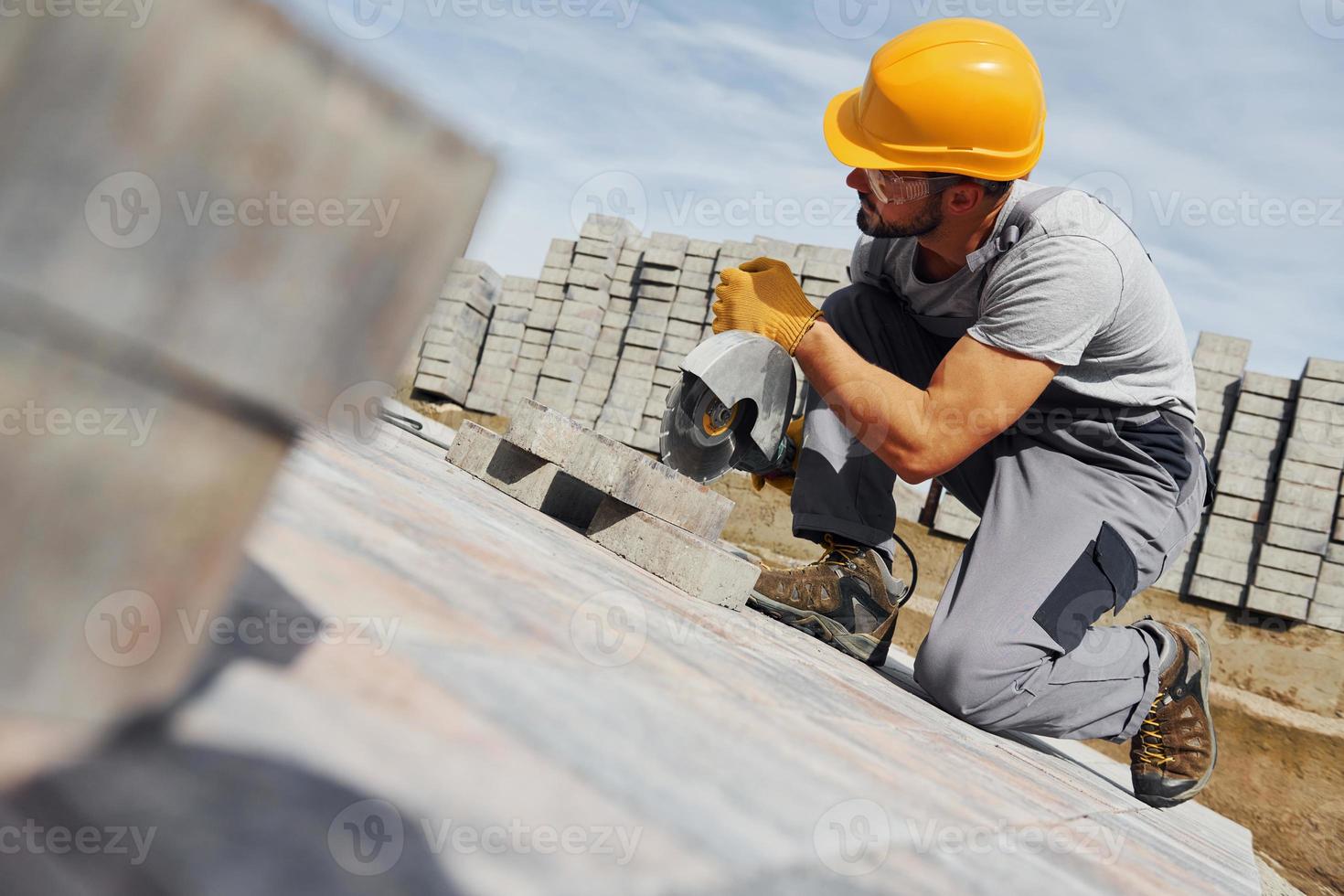 Slicing by circular saw. Male worker in yellow colored uniform have job with pavement photo