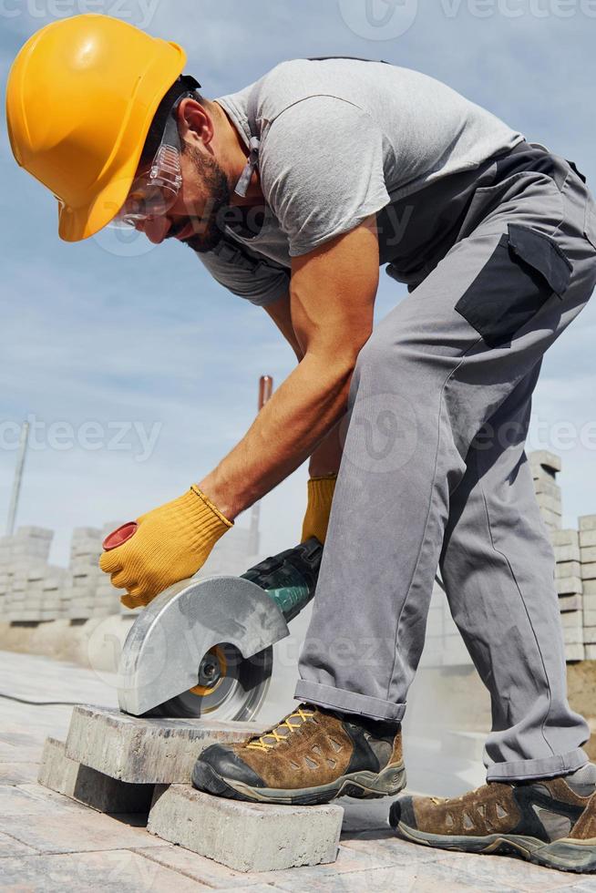 utiliza sierra circular. trabajador masculino con uniforme de color amarillo tiene trabajo con pavimento foto