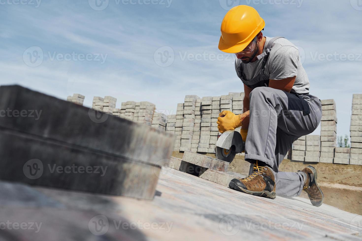 Slicing by circular saw. Male worker in yellow colored uniform have job with pavement photo