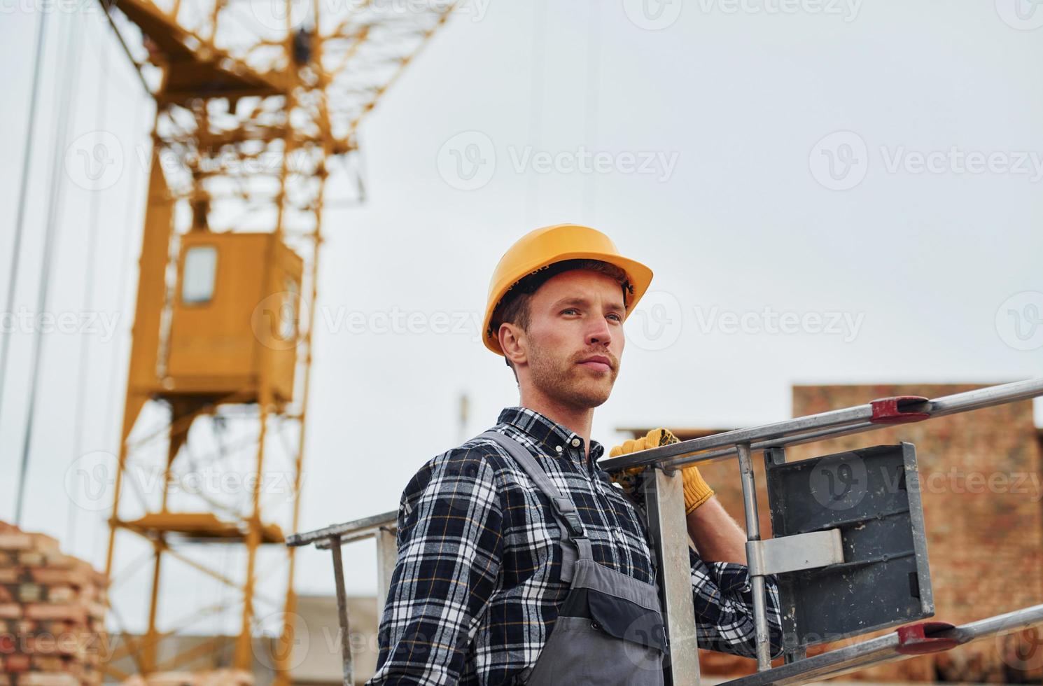 Ladder in hands. Construction worker in uniform and safety equipment have job on building photo