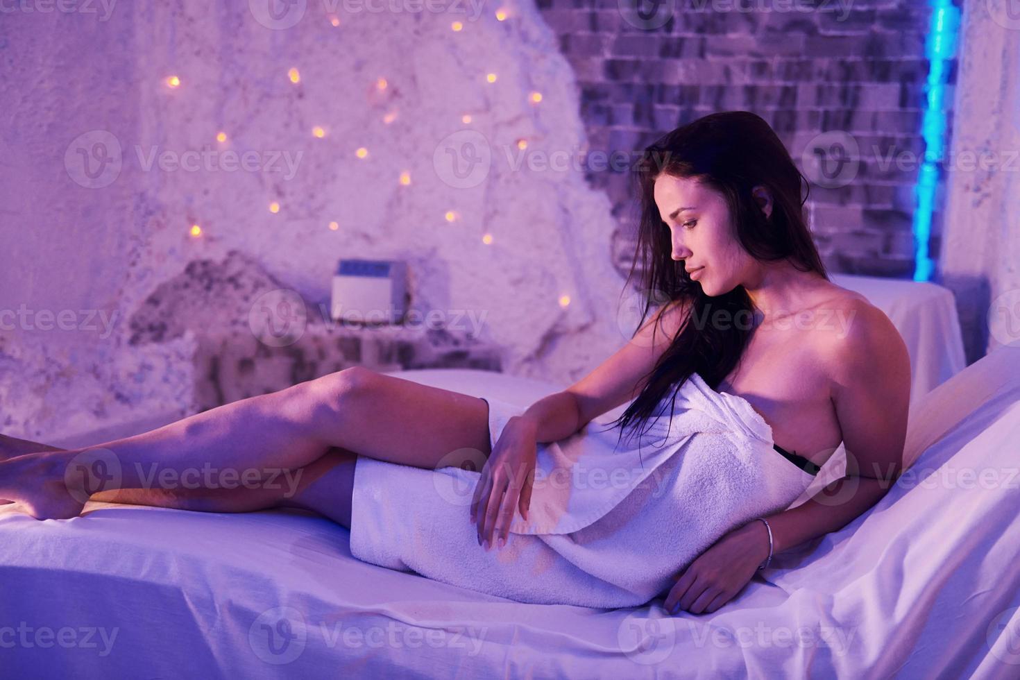 Young woman in white towels lying down on beds indoor in room with violet decor photo