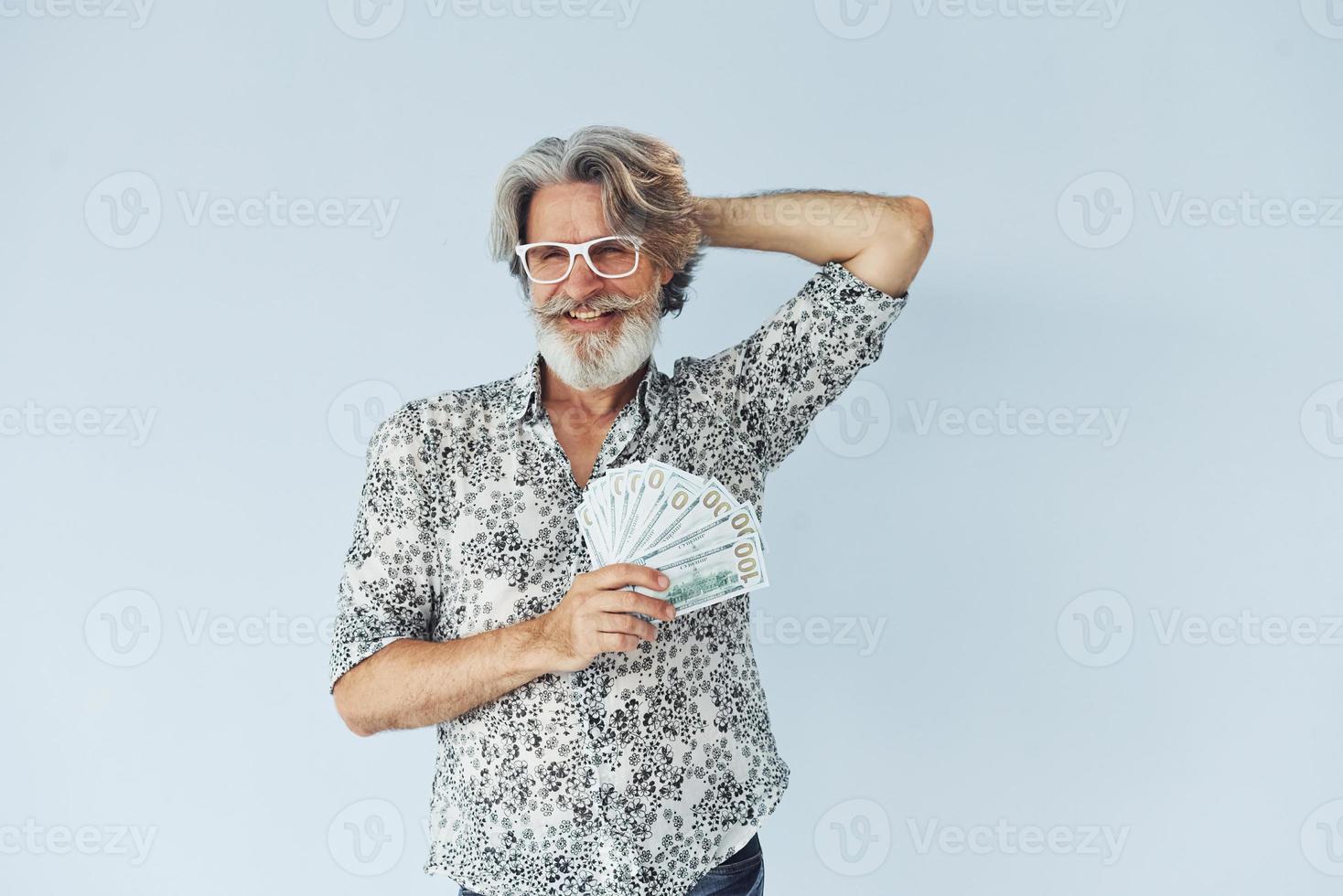 Senior stylish modern man with grey hair and beard indoors and holds cash photo