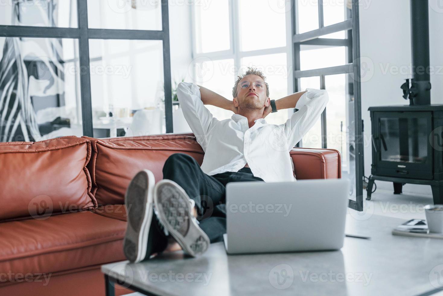 With laptop. Caucasian young guy in elegant white shirt indoors at home photo
