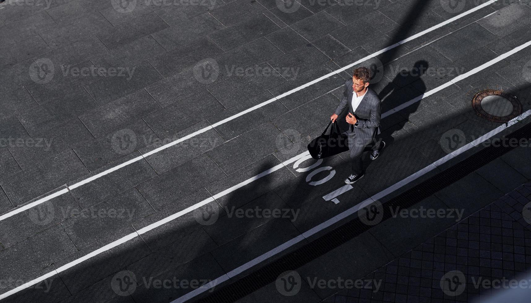 Young successful businessman in grey formal wear is outdoors in the city photo