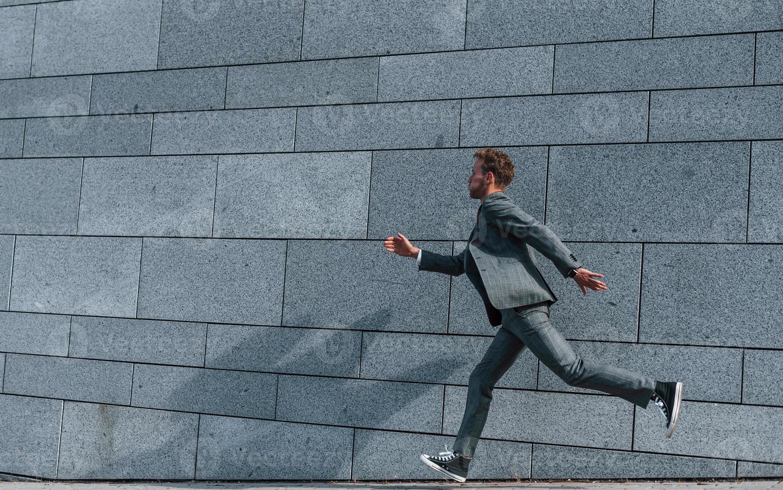 Running and late for the work. Young successful businessman in grey formal wear is outdoors in the city photo