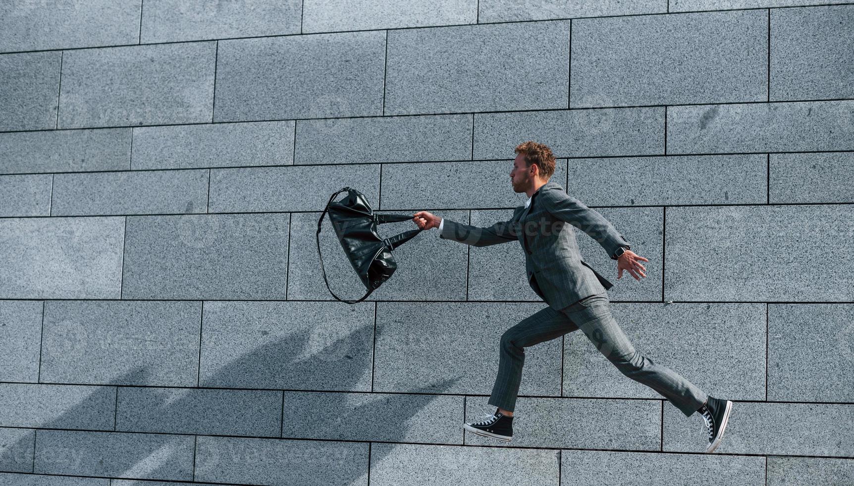 corriendo y tarde al trabajo. joven empresario exitoso en ropa formal gris está al aire libre en la ciudad foto