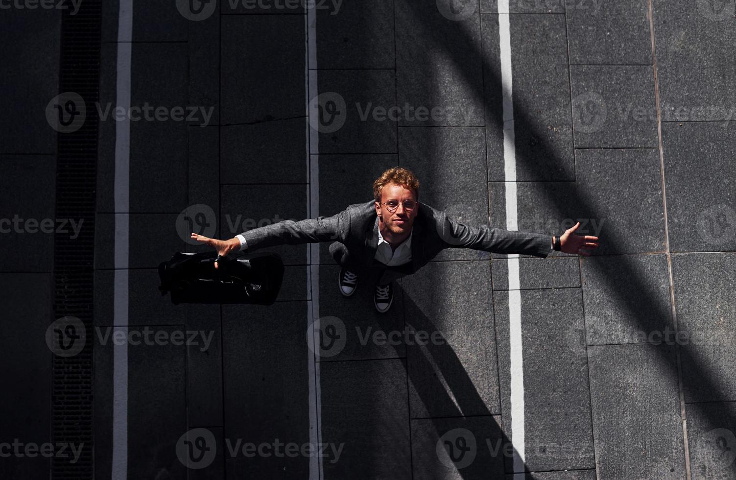 Celebrating success. Young businessman in grey formal wear is outdoors in the city photo