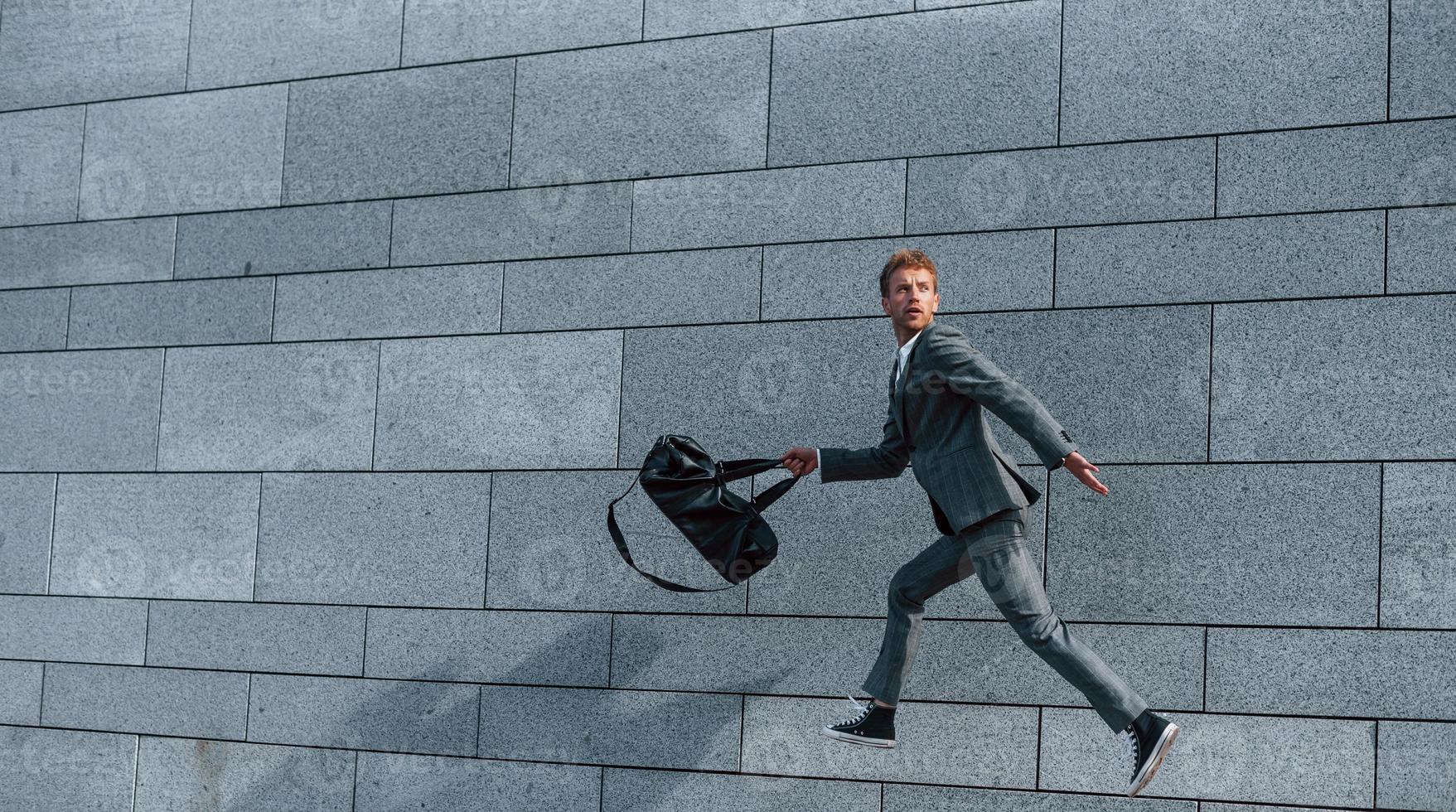 Running and late for the work. Young successful businessman in grey formal wear is outdoors in the city photo