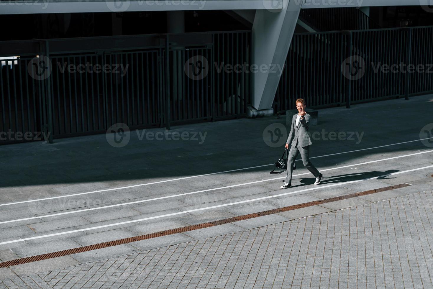 muestra el dedo medio. joven empresario exitoso en ropa formal gris está al aire libre en la ciudad foto