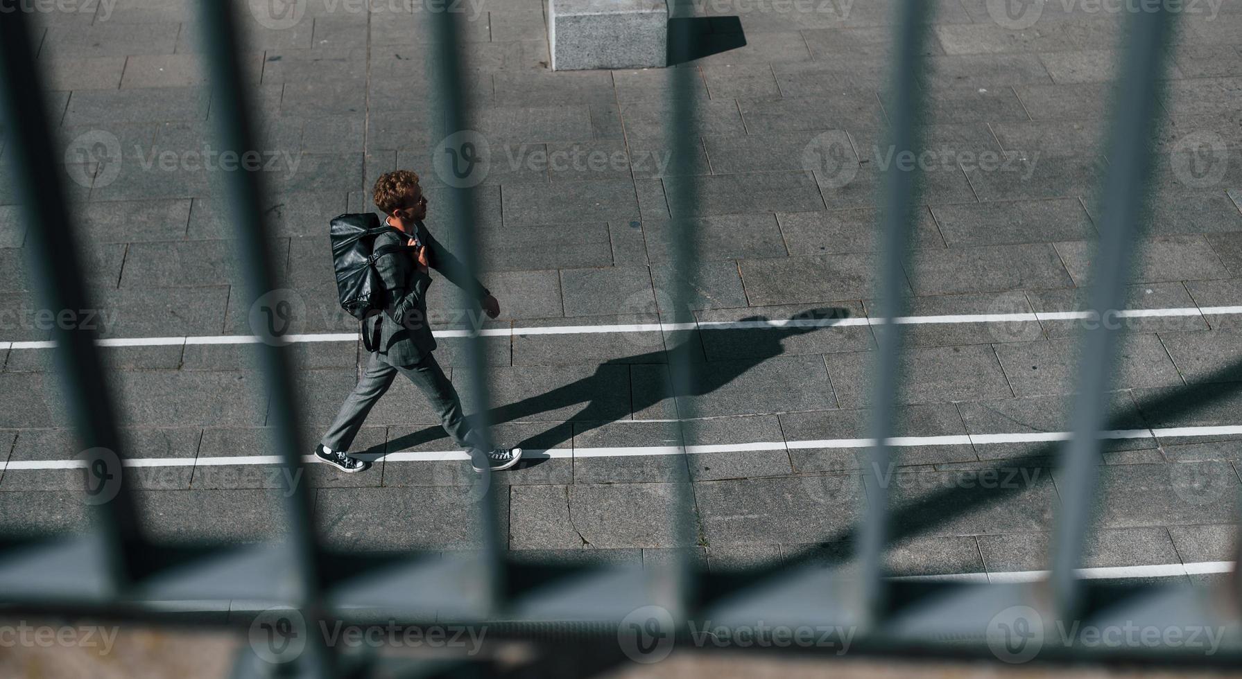 Talks by phone. Young successful businessman in grey formal wear is outdoors in the city photo