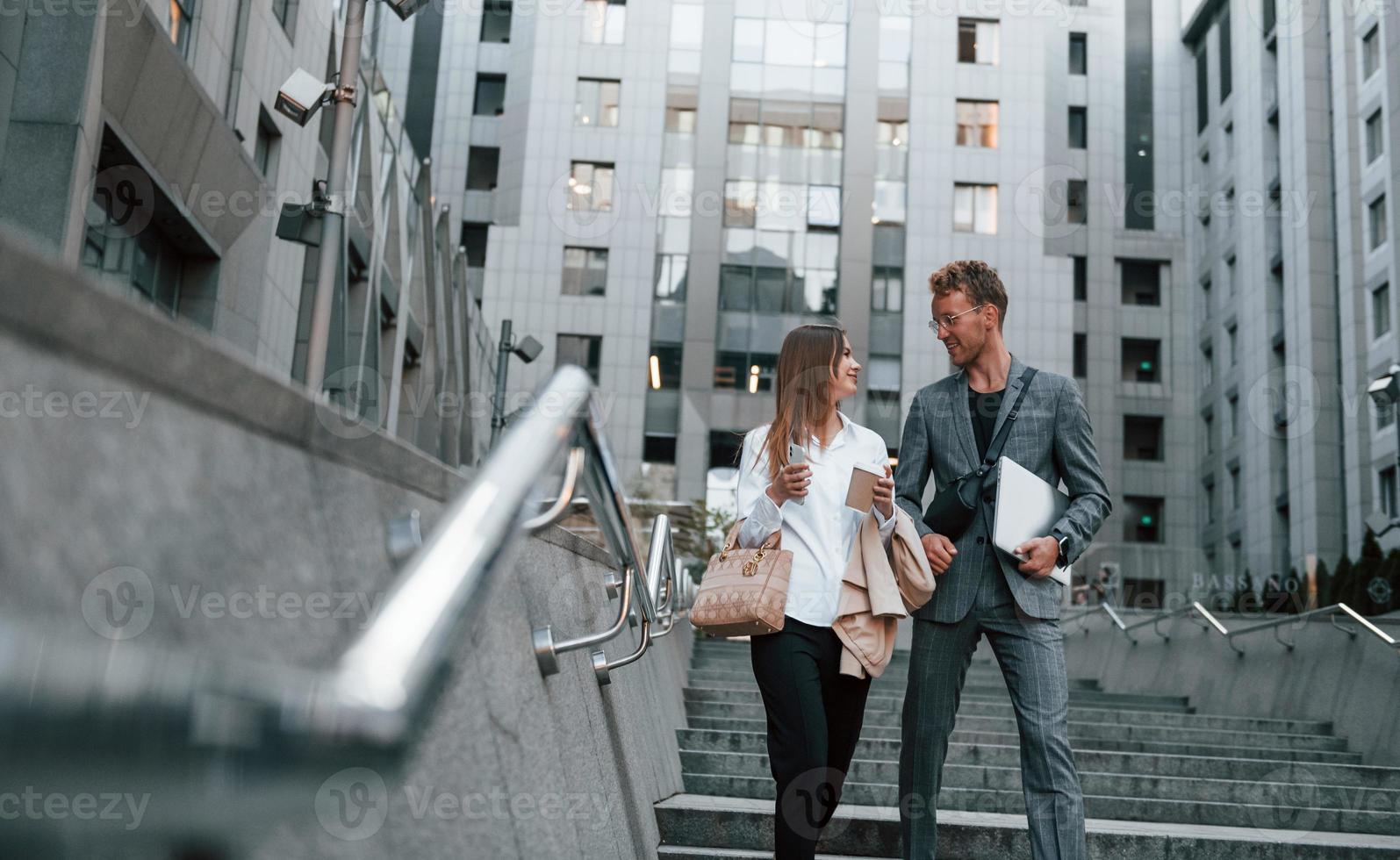 Closed laptop in hands. Woman and man in the town at daytime. Well dressed people photo