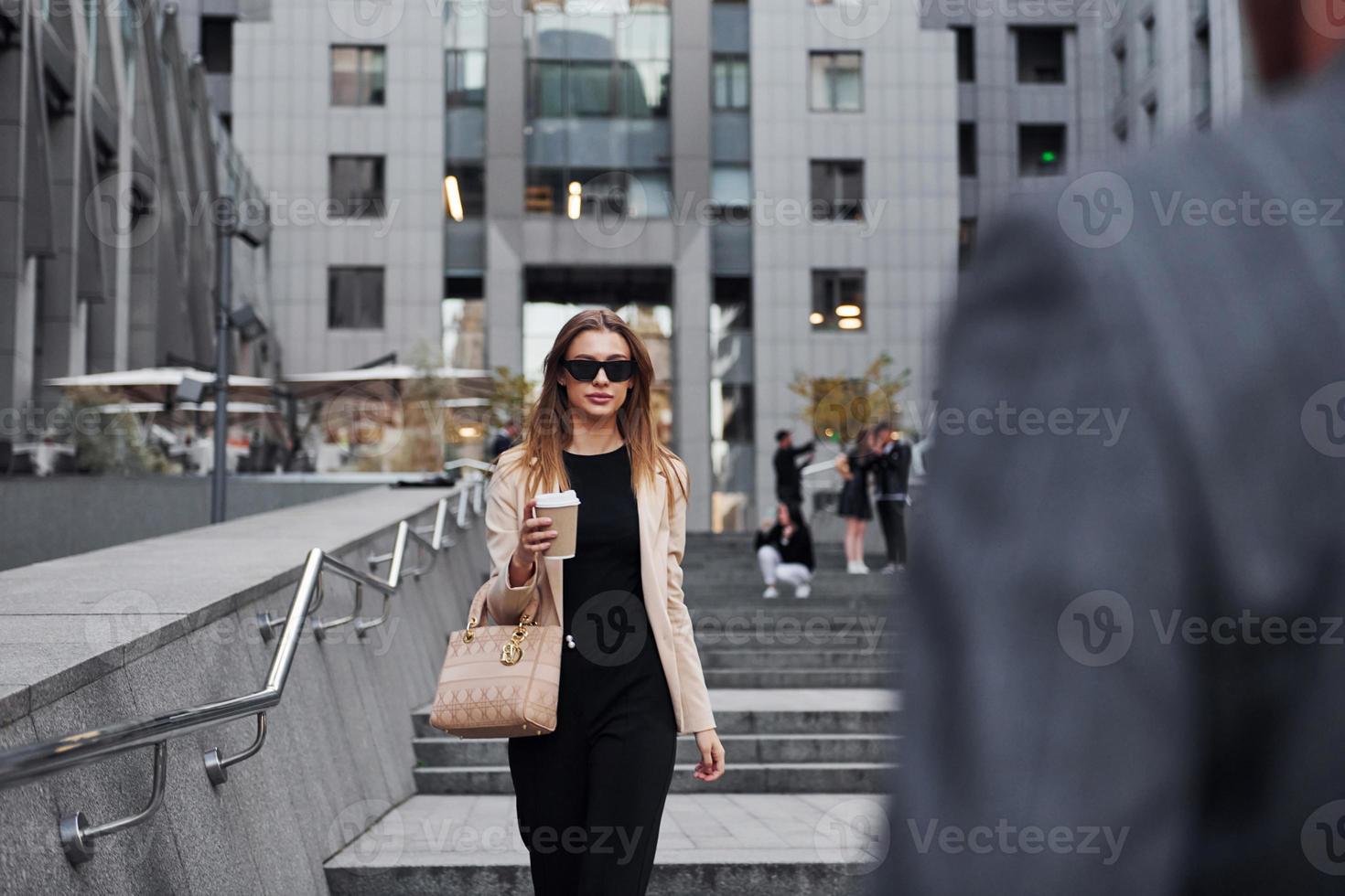 Girl holds drink. Woman and man in the town at daytime. Well dressed people photo