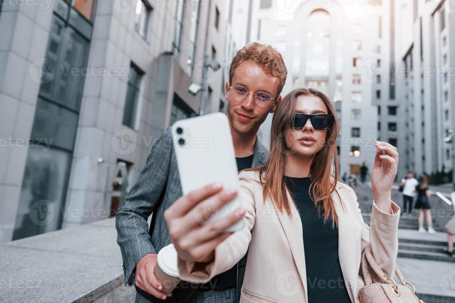 Makes selfie. Woman and man in the town at daytime. Well dressed people photo