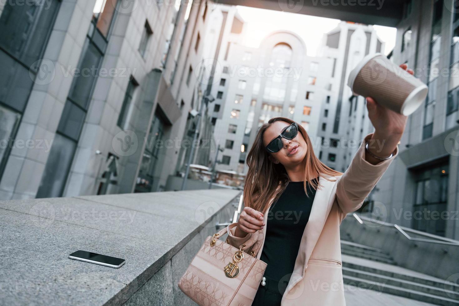 Holds cup of drink. Beautiful young european woman is outdoors in the city at daytime photo