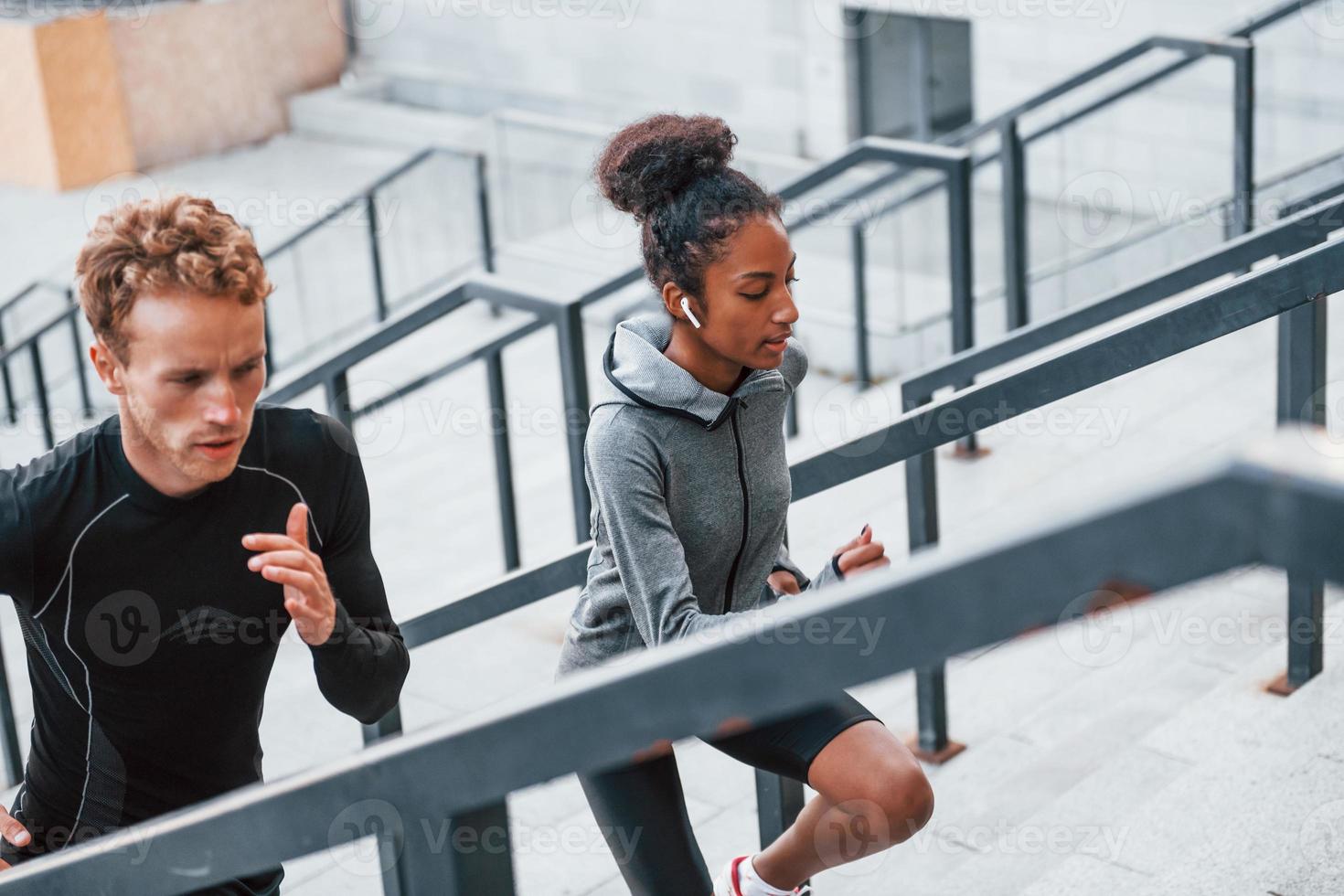 corriendo en las gradas. el hombre europeo y la mujer afroamericana en ropa deportiva hacen ejercicio juntos foto