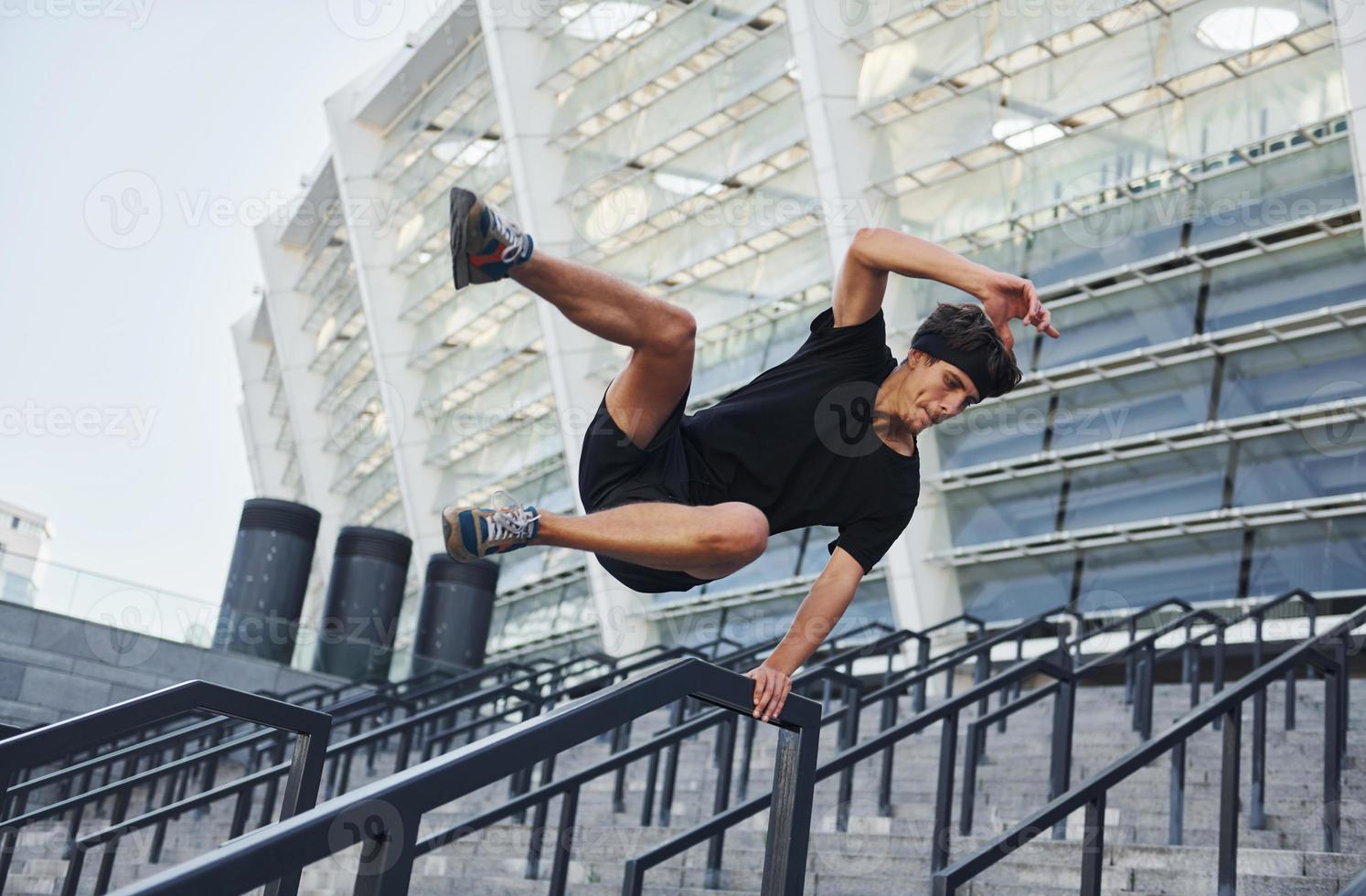 Does parkour. Young man in sportive clothes have workout outdoors at daytime photo
